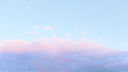 Obraz premium A serene sky showcases soft pink and blue clouds as the sun sets in the evening, creating a tranquil atmosphere just before darkness falls, perfect for reflection.