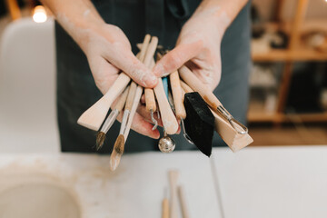 Potter holds craft instruments for clay sculpting. Wooden craft tools for molding ceramic crockery.