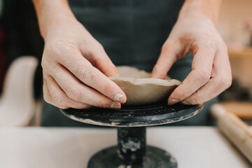 Hands shaping clay into dish in the craft studio close-up. Artisan sculpts ceramic bowl using...