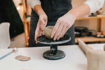 Hands shaping clay into dish in the craft studio close-up. Artisan sculpts ceramic bowl using potter's wheel.