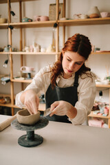 Craftswoman carefully molds a clay bowl on the potters wheel. Creating ceramic crockery in the workshop.