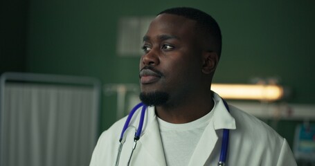 Standing in a hospital room, a young African doctor initially looks serious dressed in a white coat...