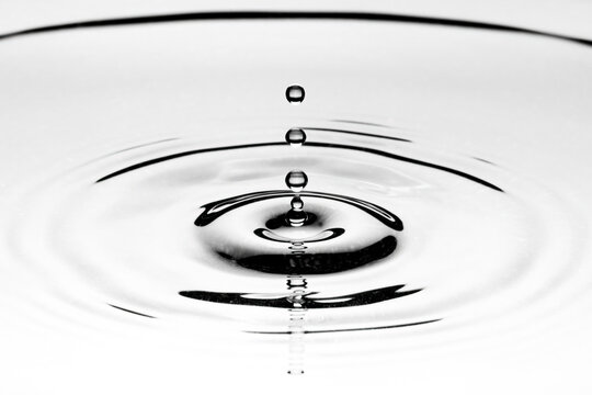 Black and white closeup shot on a drop of water hitting the surface of a water puddle taken with flash in studio