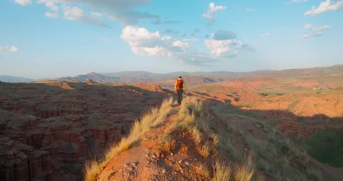 A traveler explores by walking on the rocky ridge at Narman Fairy Chimneys in Erzurum. Red rocks and valleys offer a fascinating view at sunset.