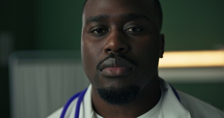 Young African doctor, dressed in a white coat with a stethoscope, gives a serious look.