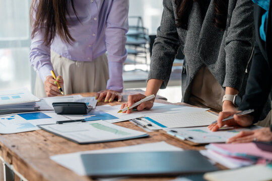 Professional women collaborating, reviewing financial data on charts and graphs, discussing investment strategies with calculator and pens during strategic workplace conference
