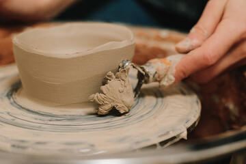 Creating ceramic earthenware on the manufacturing. Artisan forms clay pot with potters tool on the spinning wheel.