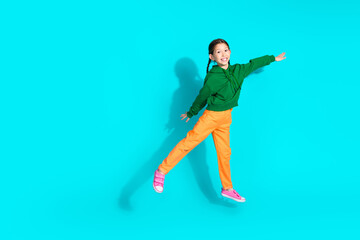 Obraz premium Adorable young girl in orange pants and green hoodie smiling brightly against teal background