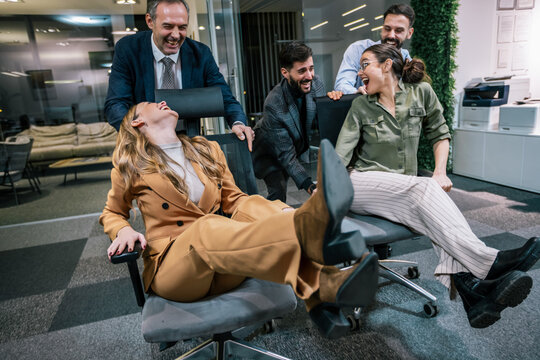 Playful scene in a modern office with businesspeople engaging in a friendly competition. In the image, colleagues are playfully pushing each other on office chairs.