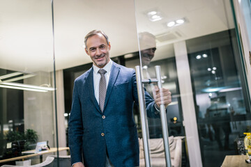 Senior businessman opening the glass doors to his office. He is dressed in formal business attire
