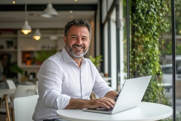 A man is sitting comfortably at a table while using his laptop computer