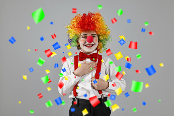 Happy boy dressed like clown under falling confetti on grey background. Party time
