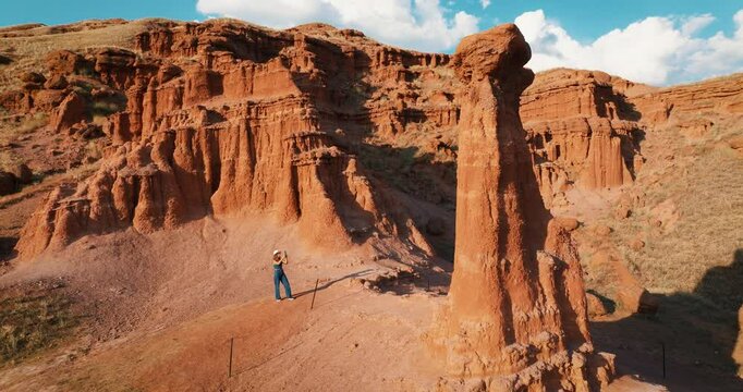 The red fairy chimneys in the Narman district of Erzurum are impressive rock formations shaped by wind and rain. A woman takes a photo. The camera pans around the formation.