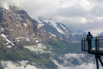 Tourist standing on the edge of the cliff skywalk in First, Grindelwald, opposite the majestic North Face of Eiger & enjoying the panorama of alpine mountains in Bernese Oberland, Switzerland, Europe