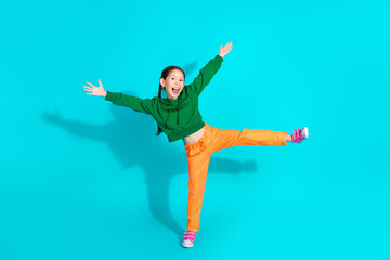 Energetic young girl in vibrant clothing dancing joyfully against turquoise background