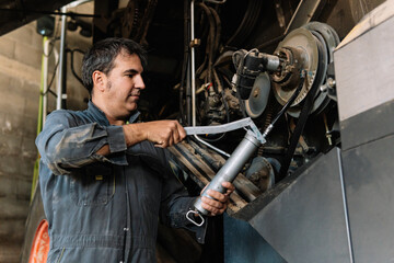Farmer greasing combine harvester with grease gun during maintenance in garage