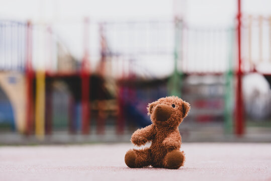 Children toy,A lost teddy bear sitting alone in playground floor in gloomy day use for Loneliness,Kidnap or Missing children day banner,Lonely and sad brown bear doll lied down alone in the park