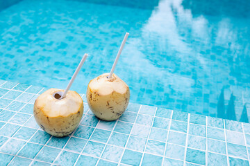 A fresh coconuts with a straw lies on the side of the pool. A delicious tropical drinks