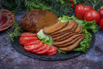 Vegan seitan roast slices with tomato slices on lettuce leaves on slate plate