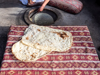 woman peels baked lavash from wall of tandoor