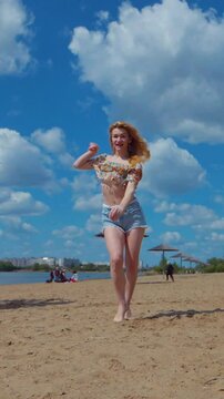 Vertical. Woman dancing bachata, salsa and kizomba on the beach against the background of the blue sky. Smiling Woman barefoot poses and dances seductively on hot sand. Beach scene with girl enjoying 