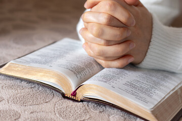 Fototapeta premium Christian woman is praying and studying from open holy bible book. Close-up. Selective focus. Praise, thanksgiving, and faith in God Jesus Christ, biblical concept.