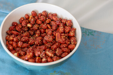 Candied peanuts in a white bowl on table with blue placemats and white tablecloth. Snack ready to serve