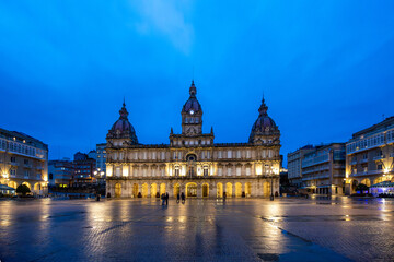 Night view of Plaza María Pita in A Coruña, Galicia, with its illuminated architecture reflected on the wet ground after the rain. 
