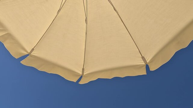 White beach umbrella. Blue sky in the background. View from below. Relaxing context. Summer holidays by the sea. General contest and location