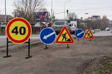Brightly colored traffic signs indicate a speed limit and direct drivers among ongoing road work in...