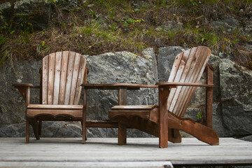A view of a pair of rustic wood Adirondack chairs on a wood deck.