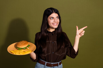 Smiling young woman holding a plate with a burger and fries against khaki background