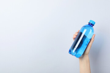 Woman holding plastic bottle of water on light background, closeup. Space for text