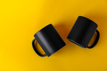 Two blank black mugs on yellow background, top view. Mockup for design