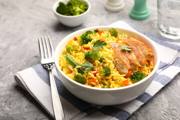 Tasty rice with vegetables and chicken served on grey table, closeup