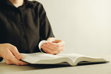 Woman reading Holy Bible in English language at beige table, closeup