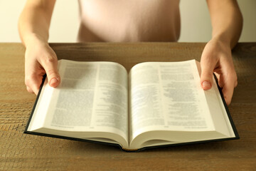 Woman reading Holy Bible in English language at wooden table, closeup