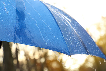 Open blue umbrella under pouring rain outdoors, closeup