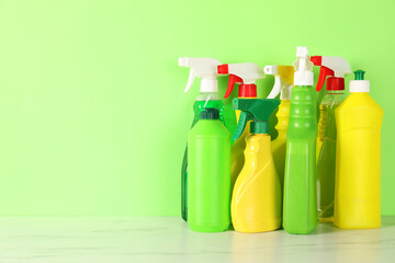 Different cleaning products on white marble table against green background, space for text