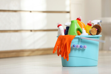 Bucket with different cleaning supplies on floor in bathroom, space for text