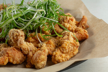 A closeup view of a basket of Korean fried boneless chicken, topped with scallion shreds.