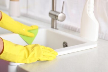 Woman cleaning sink with rag in kitchen, closeup