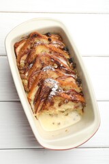 Freshly baked bread pudding in baking dish on white wooden table, top view