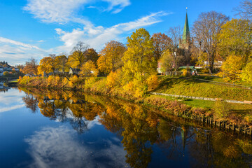Beautiful autumn foliage along Nidelva River with the tower of the 750 years old Nidaros Cathedral at the back in Trondheim Municipality in Trondelag county, Norway