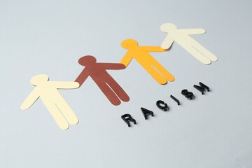 Word Racism and human paper figures of different colors on light grey background, closeup