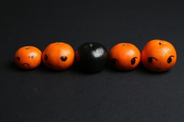 Stop racism. One black tangerine among orange ones on black background, closeup