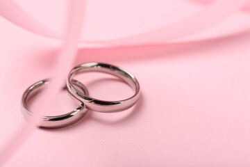 Wedding rings and ribbon on pink background, closeup. Space for text