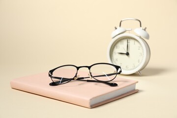 Alarm clock, glasses and book on beige background, closeup. Time for knowledge