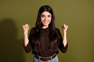 Confident young woman celebrating success with fists raised, standing against khaki background