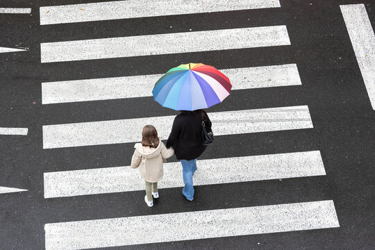 Mother and daughter crossing the street on pedestrian crossing during a rainy day